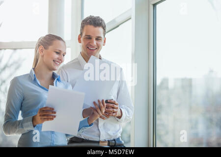 Glückliche junge Unternehmerin und Unternehmer diskutieren über Dokumente im Büro Stockfoto