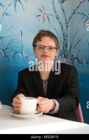 Ein junger Mann mit Down-syndrom sitzt an einem Tisch in einem Cafe Kaffee trinken Stockfoto