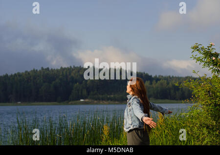 Seine Arme am Ufer des Sees geöffnet, drehte sein Gesicht in den Wind, eine einsame junge Frau, Stockfoto