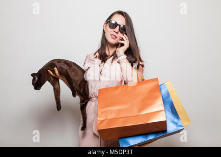 Schlankes Mädchen mit den schwarzen Brille mit schwarzen Katze und Handy trägt Kleidung Taschen Stockfoto