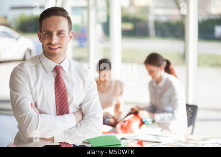 Portrait von selbstbewussten jungen Geschäftsmann mit weiblichen Kollegen, die im Hintergrund bei Büro Stockfoto