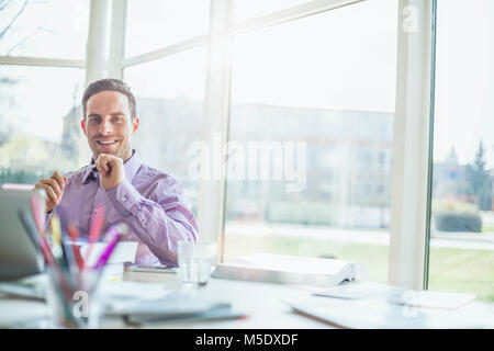 Portrait von selbstbewussten jungen Geschäftsmann am Schreibtisch im Büro sitzen Stockfoto