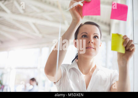 Schöne junge geschäftsfrau, Haftnotizen auf Glas Wand im Büro Stockfoto