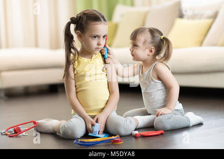 Zwei Kinder, lächelnd Kleinkind Mädchen und ihre ältere Schwester, Arzt und Krankenhaus mit medizinischen Spielzeug, Spaß zu Hause in Stockfoto
