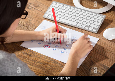 Nahaufnahme einer Frau Kreisen das Datum auf dem Kalender mit roter Farbe Markierung auf Schreibtisch Stockfoto