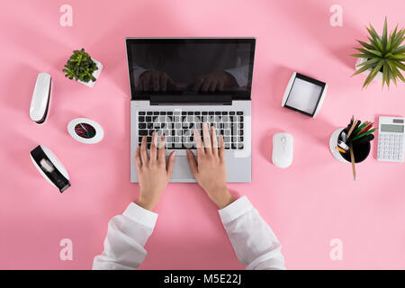 Nahaufnahme einer Frau mit Laptop auf Rosa Schreibtisch am Arbeitsplatz Stockfoto