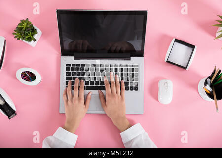 Nahaufnahme einer Frau mit Laptop auf Rosa Schreibtisch am Arbeitsplatz Stockfoto