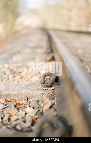 Nahaufnahme eines Metallbefestigungssystems auf einer alten Eisenbahnstrecke. Schwerpunkt auf HD-Schienenclip aus geschmiedetem Stahl: Befestigungselement verbindet Schiene mit Betonschläfer. Stockfoto