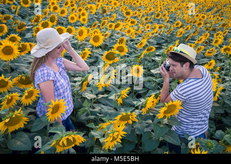 Junge hipster Kerl unter Foto von seiner Freundin mit Retro Vintage Kamera im sonnenblumenfeld. Liebe, Reisen und Sommer Konzepte. Stockfoto