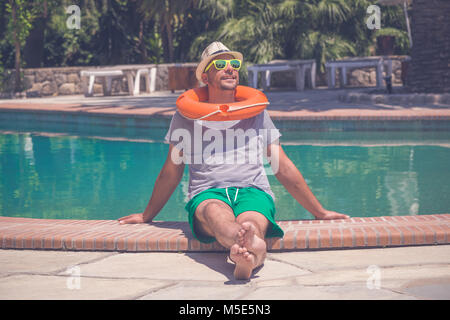 Portrait der junge Kerl mit Hut, Sonnenbrille und Rettungsring entspannend neben dem Pool. Sommer Urlaub Konzept. Stockfoto