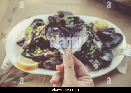 In der Nähe der weiblichen Hand öffnete Herz geformte Muschel am Tisch im Restaurant. Meer essen und gesunde Ernährung. Stockfoto
