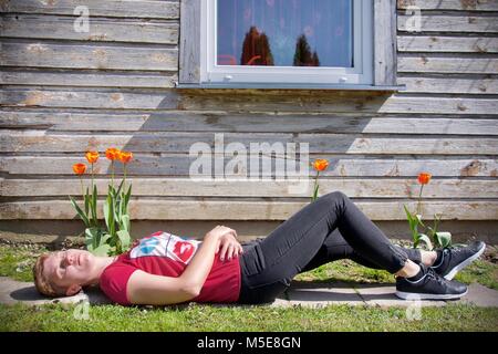 Frau Sonnenbaden auf der Liegewiese mit orangen Blüten unter einem Fenster in der Frontseite eine Holzhütte Stockfoto