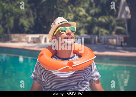 Portrait der junge Kerl mit Hut, Sonnenbrille und Rettungsring entspannend neben dem Pool. Sommer Urlaub Konzept. Stockfoto