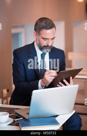 Senior älteren Geschäftsmann Ausfüllen etwas Papier arbeiten, trinken Kaffee in einem Cafe Stockfoto