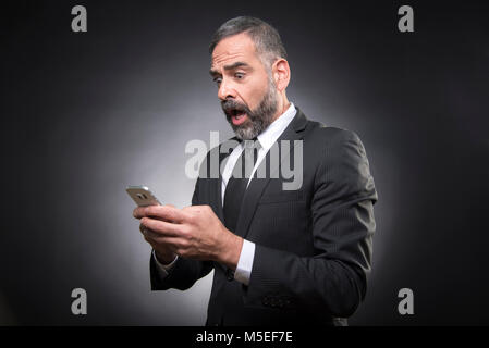Senior Business Mann insgesamt Schock mit einer Meldung, die er über sein Handy empfangen Stockfoto