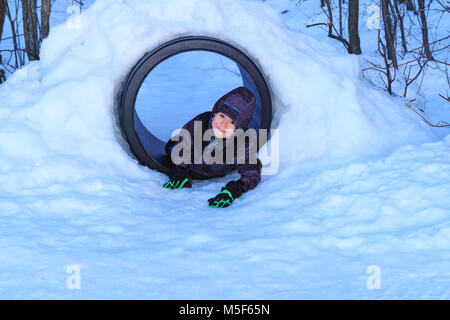 Happy Boy Spielen im Schnee Tunnel. Richtige kleine Junge hat Spaß im Schnee Installationen von öffentlichen Park. Tolle Kinder spielen draußen im Schnee. Cute Boy. Stockfoto