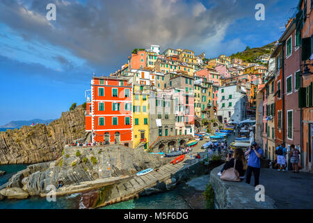 Touristen im Sommer Morgen im farbenfrohen Fischerdorfes und Hafen in Riomaggiore Italien genießen, Teil der Cinque Terre an der italienischen Riviera Stockfoto