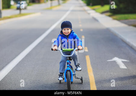 Glückliches Kind auf einem Fahrrad an der asphaltierten Straße im Frühjahr oder Herbst. Cute boy lernen Fahrrad auf einem Radweg zu fahren. Adorable kid boy Spaß haben. Stockfoto