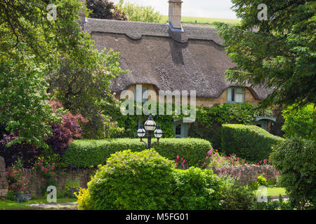 Charmante Strohdach englisches Cottage in ländlichen Landschaft von Cotswold, voll von blühenden Pflanzen, Sträuchern und Bäumen, an einem sonnigen Sommertag. Stockfoto