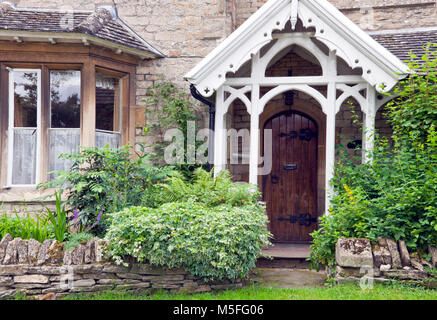 Dunkelbraun Holztüren in einem alten traditionellen Englischen Steinhaus mit Blumen und Sträucher in einem kleinen Garten mit Trockenmauern Zaun. Stockfoto