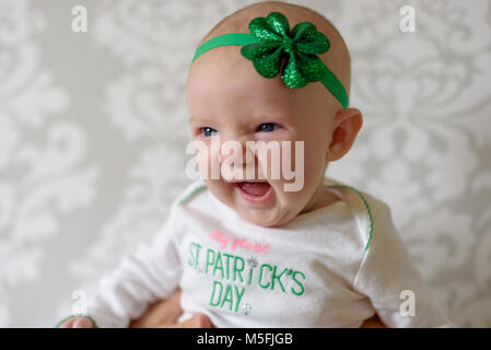 Irische Baby mit großen blauen Augen lachen und tragen St Patricks Day Outfit und shamrock Kopfbügel Stockfoto