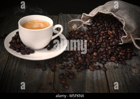 Geröstete Kaffeebohnen und Kaffee Tasse auf hölzernen Tisch Stockfoto