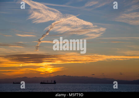 Boote am Horizont bei Sonnenuntergang unter einem bewölkten Himmel Stockfoto