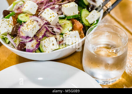 Frischer Salat, Teller, Glas Wasser auf dem Tisch, Nahaufnahme. Griechischer Salat mit Feta Käse, gesundes Essen Konzept. Stockfoto