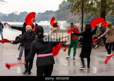 Eine Gruppe von älteren Frau mit rotem Papier Ventilatoren Praxis früh am Morgen Tai Chi am Ho Hoan Kiem See, Hanoi, Vietnam Stockfoto