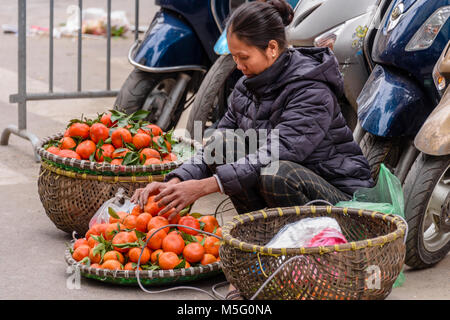 Eine Obstverkäuferin arrangiert ihren Korb und ihre Bambusstange auf der Straße in Hanoi, Vietnam Stockfoto