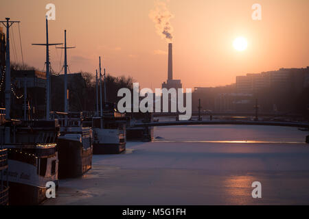 TURKU, FINNLAND - 18 Februar 2018: Golden Sunset im Winter über den Fluss Aura mit der beliebten Flussboot Restaurants auf dem gefrorenen Fluss und Turku E Stockfoto