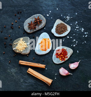 Bunten Gewürzen auf Kieselsteinen in der mittleren Gruppe mit Zimtstangen, Knoblauchzehen, Salz und Pfefferkörnern, Stockfoto