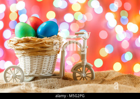 Ostern Karte, farbige Eier im Nest. Spielzeug Fahrrad mit einer Karre. Frohe Ostern. Rosa bokeh Hintergrund. Stockfoto