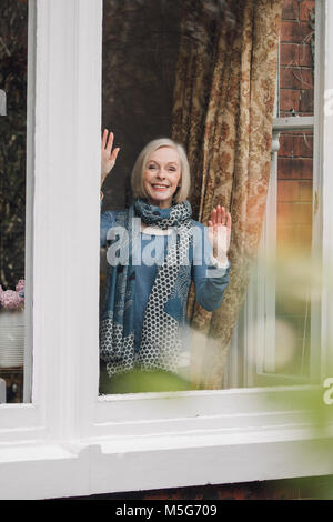 Ältere Frau ist Abschied winkend aus einem Fenster in Ihrem Haus. Stockfoto