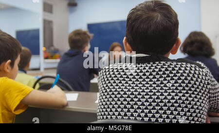 Mitschüler, die Kinder in der Schule - Junge sitzt am Tisch und Suchen während der Lehrer erklärt die Lektion Stockfoto