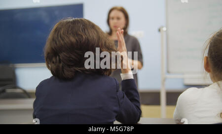 Mitschüler in der Schule - Mädchen sitzt am Tisch und Suchen während der Lehrer erklärt die Lektion Stockfoto