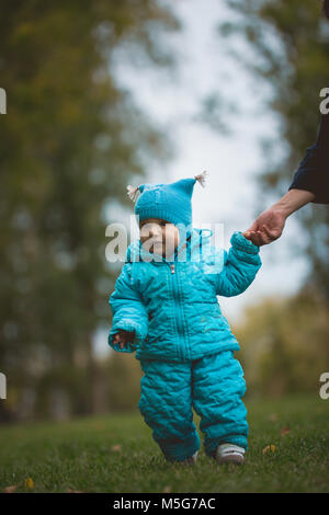 Happy Family Wandern im Herbst Park: ein Junge läuft auf dem Feld mit der Hilfe der Mutter Stockfoto