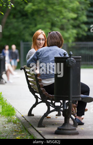 Ein Mädchen in der Brille sitzt auf einer Bank neben einer Freundin Stockfoto