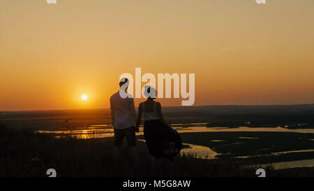 Paar-brave Junge und schöne Mädchen steht auf einem hohen Hügel suchen Silhouette Sonnenuntergang Stockfoto