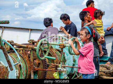 Eine junge philippinische Mädchen an Bord einer Fähre zur Insel vorgibt, mit dem Boot durch das Spielen mit alten machienery an Deck während der Fahrt von Cebu, Bohol, Ph-Antrieb Stockfoto