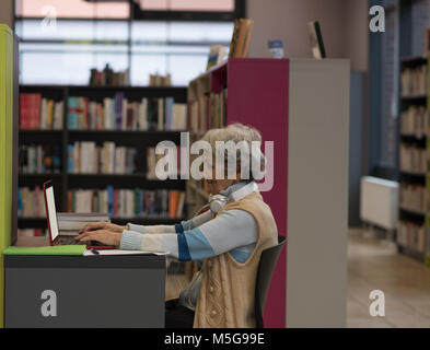 Ältere Frau mit Laptop in der Bibliothek Stockfoto