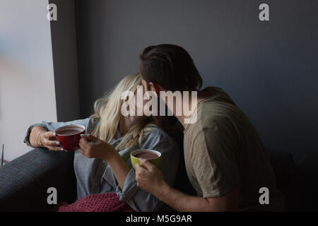 Paar einander küssen während Kaffee im Wohnzimmer Stockfoto