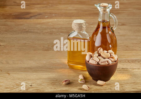 Zusammensetzung der aromatischen Öl in einem Glas und Flasche mit ungeschälte Pistazien in der Schale auf Holztisch, close-up. Nahrhafte therapeutische Nahrung für Heilen Stockfoto