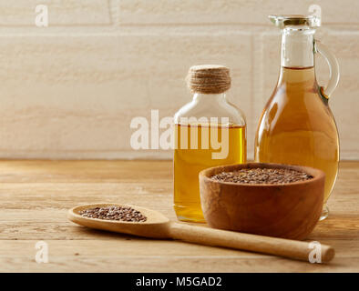 Brauner Leinsamen in Houten und Leinsamenöl in Glasflasche mit longhandled Küche Schaufel auf Braun rustikal Hintergrund, Ansicht von oben, Nahaufnahme, Stockfoto