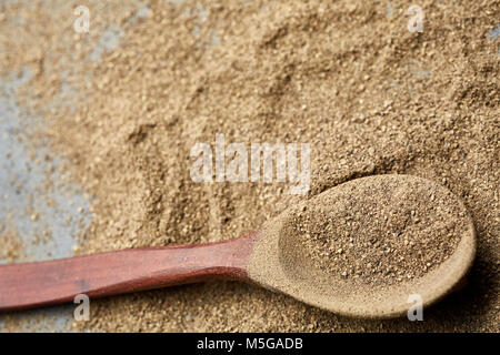 Ansicht von oben in eine braune hölzerne Löffel voll von Schleifen schwarzer Pfeffer auf das Essen strukturierten Hintergrund, geringe Tiefenschärfe, Nahaufnahme, Makro. Stockfoto