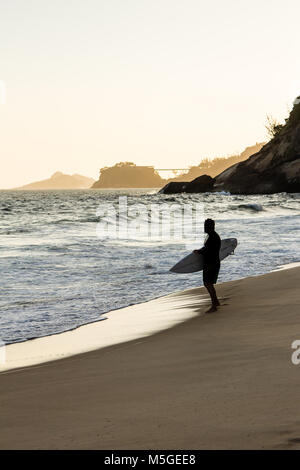 Silhouette der Surfer zu Fuß am Strand bei Sonnenuntergang Strand in Barra da Tijuca, Rio de Janeiro Stockfoto