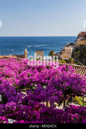 Positano durch rosafarbene Bougainvillea und Boote im Hintergrund eingerahmt. Bunte Positano, das Juwel der Amalfi Küste, mit seinen bunten Häusern und Stockfoto