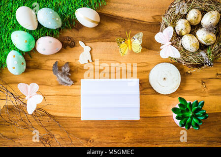 Frohe Ostern geschossen von oben als flatlay mit leeren Leuchtkasten für Begrüßungen und bunten retro Ostereier, Gras, Butterfly und Osternest auf Holz Stockfoto