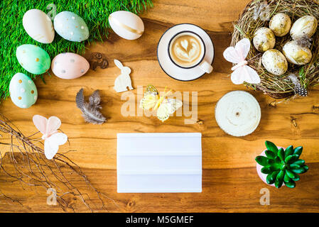 Frohe Ostern geschossen von oben als flatlay mit leeren Leuchtkasten für Begrüßungen und bunten retro Ostereier, Gras, Butterfly und Osternest auf Holz Stockfoto
