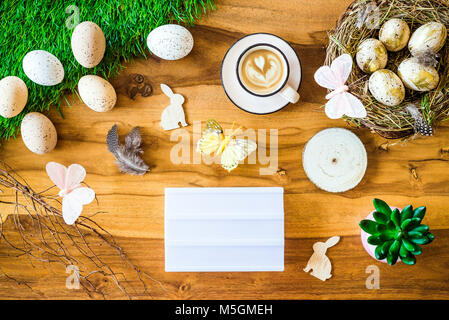 Frohe Ostern geschossen von oben als flatlay mit leeren Leuchtkasten für Begrüßungen und bunten retro Ostereier, Gras, Butterfly und Osternest auf Holz Stockfoto